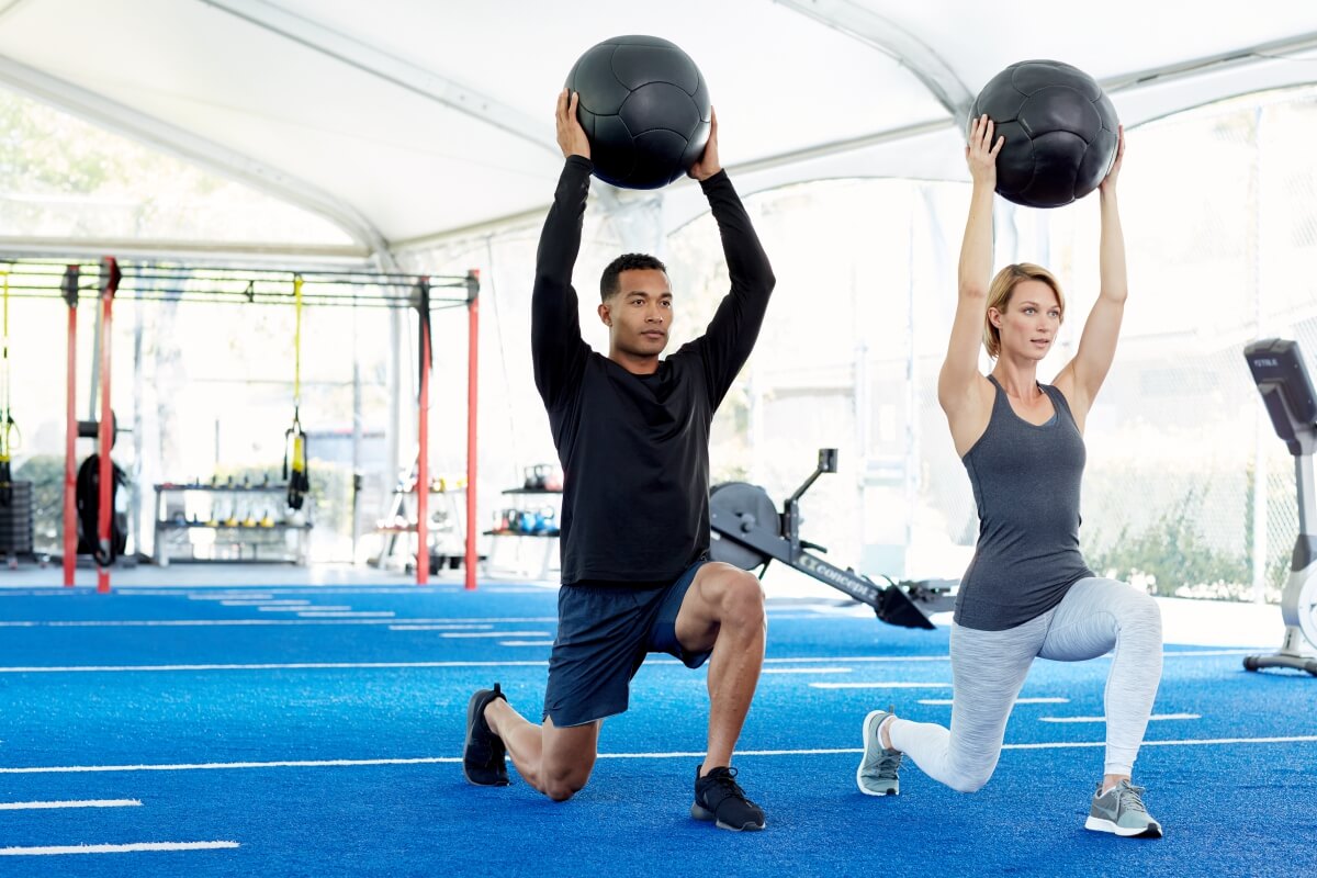 Young man and woman lunging with medicine balls