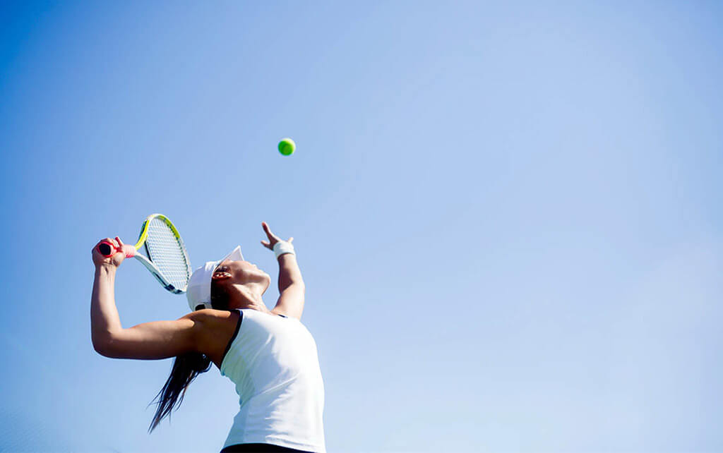 A woman serves a tennis ball while social distancing