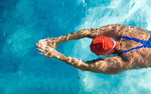 a woman wearing a red swim cap does laps at an aquatics center in goleta